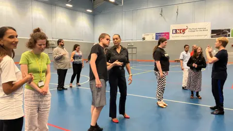 People taking part in a group activity on an indoor sports court, with participants spread across the floor and interacting in small groups.