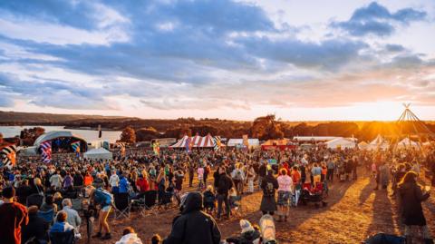 A crowd of people at a festival at sunset 