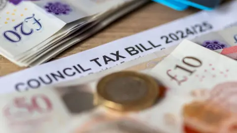 A council tax bill for 2024/25 is covered by money including £20 and £10 notes and a £1 coin.