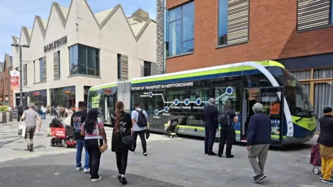Hertfordshire County Council People outside of the Harlequin shopping centre in Watford gather to see the bus that looks like a tram.