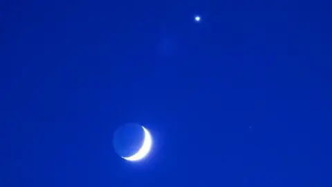 Maggie T Howlett A crescent moon and Venus against a royal blue sky