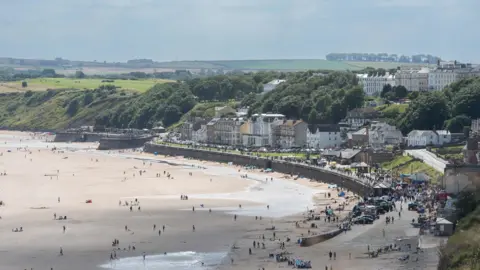 A view of Filey beach from afar. People can be seen on the beach in the sunshine.