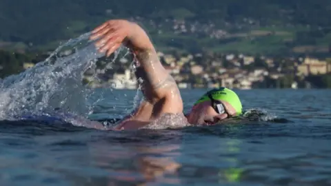 Jamie Hancock Neil Gilson is wearing a green swimming cap and goggles and his right arm is in the air mid stroke, with water flowing from his hand.