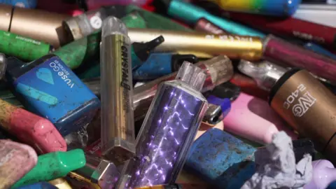 A collection of colourful vapes covered in mud.