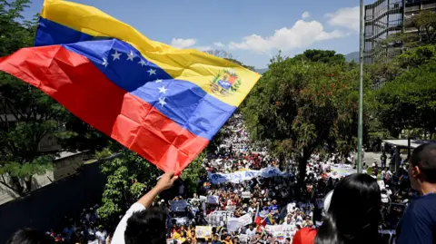 A man waves a Venezuelan flag in front of a large crowd of people