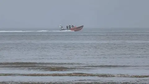 An orange RIB lifeboat on the sea, with three crew members on board.