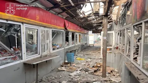 Photo provided by the Ukrainian prosecutor's office showing badly damaged indoor market area - a corridor with kiosks on either side with broken windows, and metal and glass strewn across the floor.