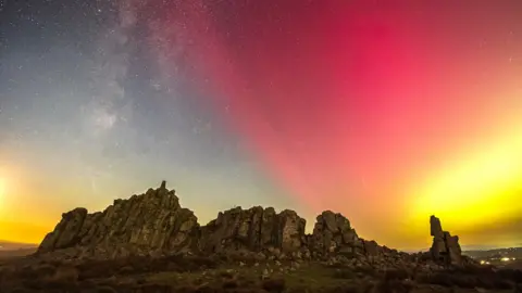 Andrew Fusek Peters Northern Lights over the Stiperstones in Shropshire. Sheets of red and yellow appear in the sky over a rocky hilltop crag on an otherwise clear night