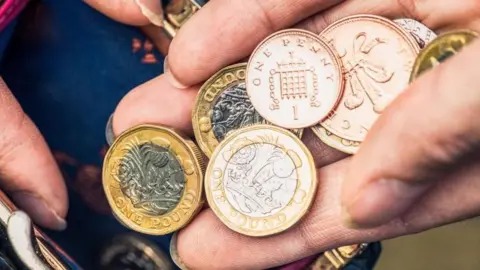 Very close up on a hand holding one pound coins as well as one and two pence pieces.