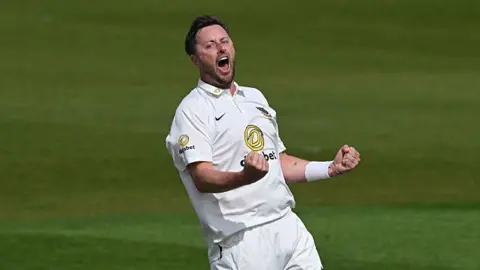 Ollie Robinson, wearing cricket whites, roars and punches both fists in celebration
