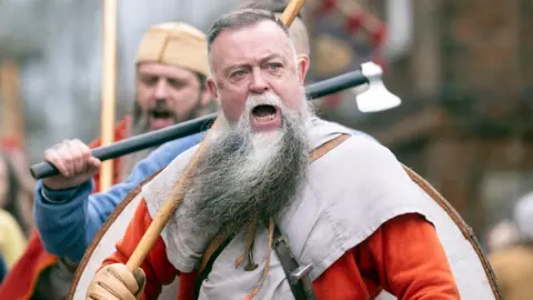 Danny Lawson/PA Wire Viking re-enactors during the Jorvik Viking Festival in York. A man with short grey hair and long beard shouts while wearing costume
