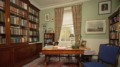 Nick Hugh McCann The Byron Room at Burgage Manor. An office room is lined with old wooden bookshelves and a wooden desk