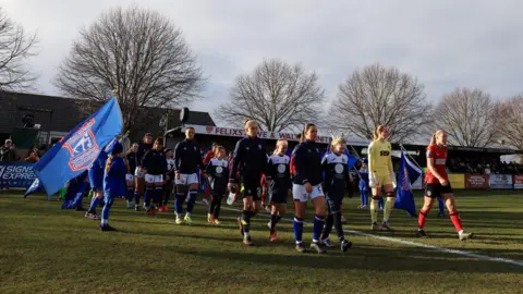 Two football teams are going to the stadium, with children like a mask alongside them. There are the large blue flags in Ipsuic, which is moved while passing.