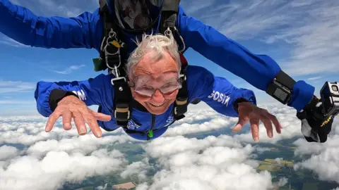Alan, with grey hair, in the air during his skydive.