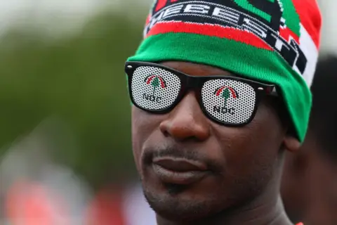 NIPAH DENNIS / AFP A supporter of the Ghana main opposition party National Democratic Congress (NDC) wears party gadget glasses with NDC written on the lenses during the electoral manifesto launch ahead of the 2024 presidential election.