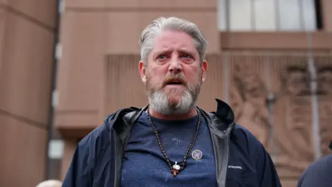 PA Media Tim Edwards, who has grey hair swept backwards and a grey beard, speaks to the camera outside Liverpool Crown Court with a serious, angry expression on his face