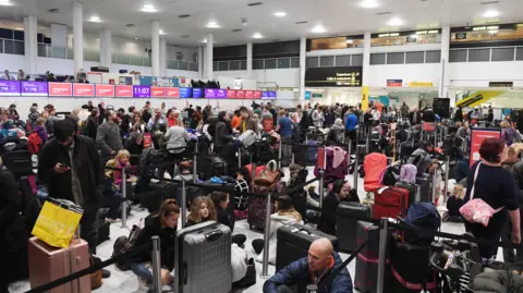 Gatwick Airport check-in hall crowded with people with suitcases and baggage trolleys. 