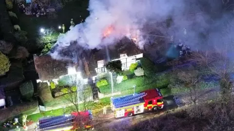 Paddy Butler Drone image of the thatched cottage on fire, surrounded by fire engines. Flames and smoke can be see coming from the roof.