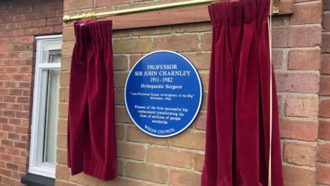 Photograph of a blue plaque on a brick wall at Wrightington Hospital