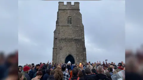 Crowd around the base of Glastonbury Tor with a grey sky