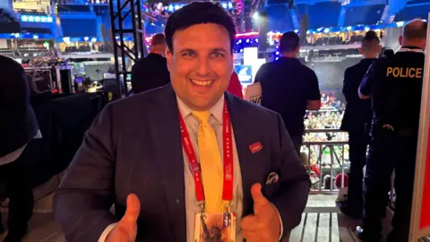 Matt smiles in a suit and gives a thumbs-up sign at the Republican convention