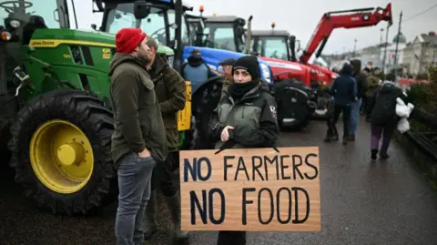 Getty Images A pistillate  dressed successful  a greenish  and achromatic  rainfall  overgarment  holds a motion   saying No Farmers No Food. A assemblage  of radical   and Green, reddish  and bluish  tractors are successful  the background.