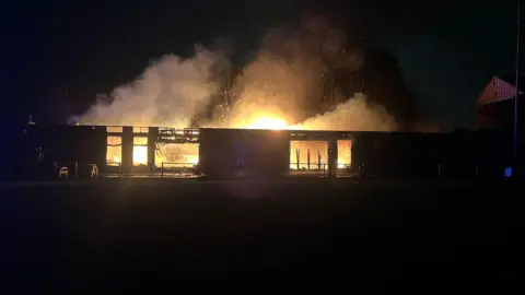 Alison Jones A low-rise building on fire; it is night-time and flames and smoke can be seen billowing from the clubhouse