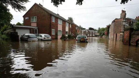 PA Media A flooded street in Beverley in 2007. An abandoned silver car floats in the water