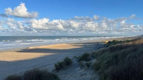 PA Media A sandy beach in Belgium with dunes in the foreground, with a view of the Channel coast in the distance.