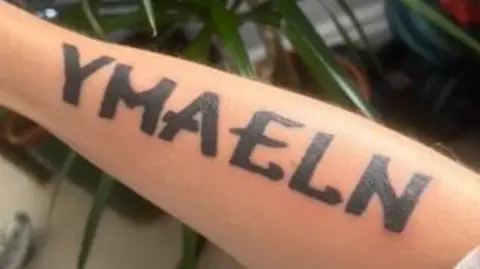 A close up picture of an arm with the tattoo of the word 'Ymaeln'. 