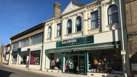 Baldwins Department Stores Ltd An image of the outside of Baldwins' Stowmarket store taking from across the road. The shop has a green sign which reads Baldwins.