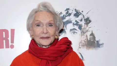 Sian Phillips is seen wearing a bright red jacket and scarf