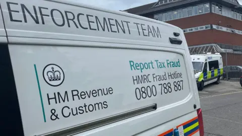 An HMRC enforcement van is parked close to a police vehicle
