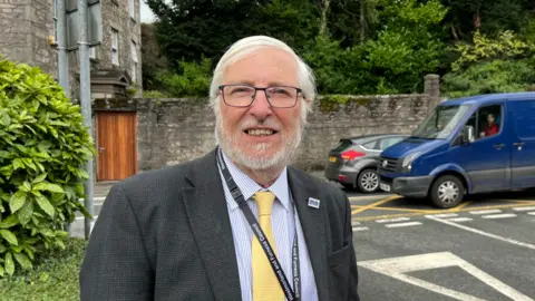 Westmorland and Furness Councillor Peter Thornton wearing a suit and lanyard with the local authority name on it.