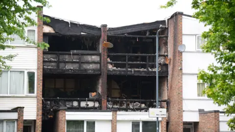 PA Media The image shows two adjoining properties that have been burnt out. The frames of the buildings are charred.