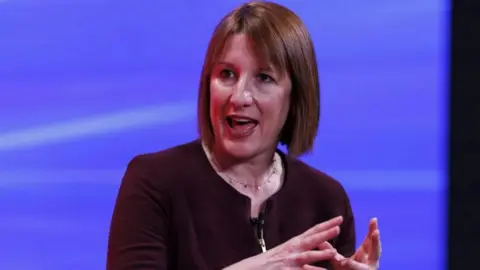 Getty Images Rachel Reeves wearing a burgundy jacket in the middle of speaking. 