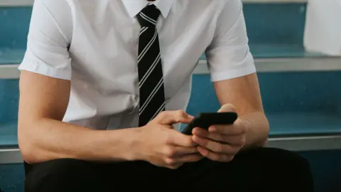 A student sits on steps in a school and uses a mobile phone