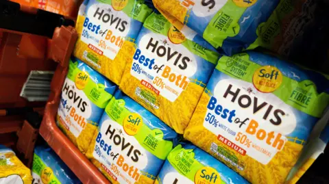 Loaves of Hovis' "Best of Both" bread stacked on top of one another in a brown crate. The wrapper states that there is 50% white flour and 50% wholemeal. 