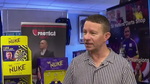 Karl Holden in his shop, surrounded by images of Luke Littler