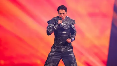 Kyle Alessandro performing on stage wearing a futuristic grey chain armour suit.