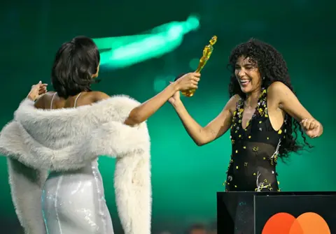 Getty Images Olivia Dean dances up to Maya Jama as she collects her award. 