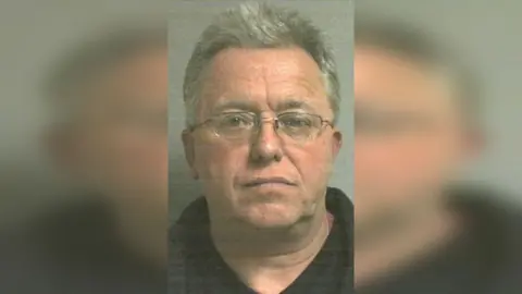 Custody photograph of Larry Roberts he has short white hair and is wearing glasses and a dark shirt