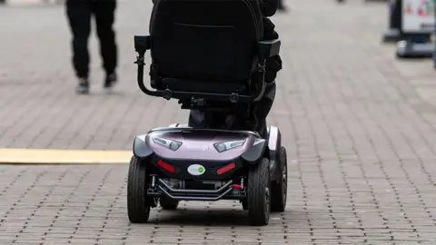 ADAM VAUGHAN/EPA-EFE/REX/Shutterstock Rear view of the bottom of a mobility scooter riding along a cobbled walkway