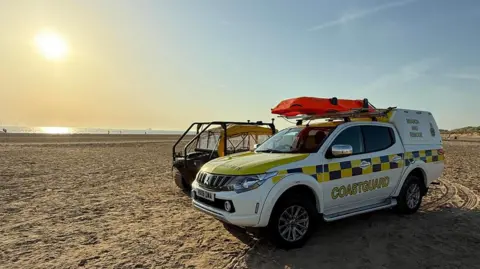 HM Coastguard Crosby Two coastguard vehicles on a sandy beach as the sun goes down over the sea