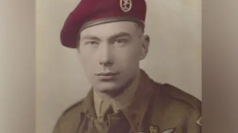 Barbara Forey A colourised sepia-toned photo of Bert Bowman in Glider Pilot Regiment uniform. He is wearing a red beret and a uniform tunic over a shirt and tie. He has very short hair and is looking at the camera. 