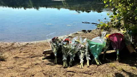 Bouquets of flowers left on sand by a lake. 
