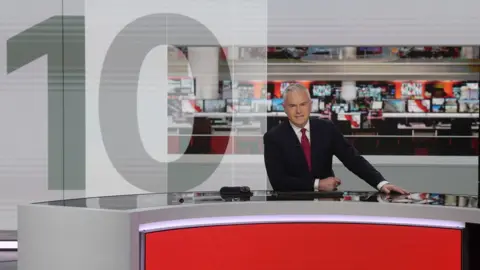 Huw Edwards na mesa de notícias ao lado de um grande "10" no logotipo do News at Ten