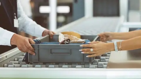 Getty Images: Two people handle a baggage scanning tray at an airport