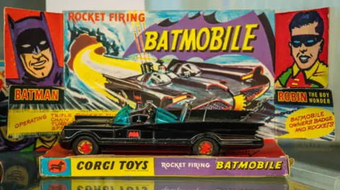 Corgi A vintage Corgi Toys “Rocket Firing Batmobile” model car in black with red bat emblems and blue‑tinted windows.