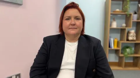 Jenny Murphy pictured with short red hair. She is wearing a navy blue blazer with a white top underneath.